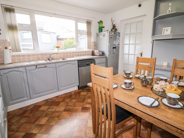 A kitchen with grey cabinets, a wooden dining table set for four, and a window overlooking a backyard. - 27 Pinewood Hill (Newry)