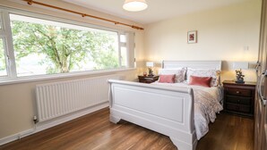 Een slaapkamer met een groot raam, een wit bed, een nachtkastje met een lamp en een radiator.