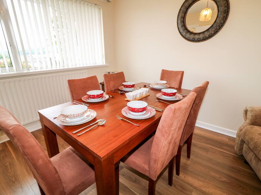 A dining room with a wooden table set for six, surrounded by six chairs.