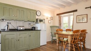 A kitchen with green cabinets, a wooden dining table with four chairs, a microwave, and a clock on the wall. - Little Trespettigue (Launceston)