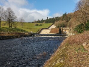 A river flowing through a rural landscape with a stone bridge and a small building. - Willow Cottage (Sheffield)