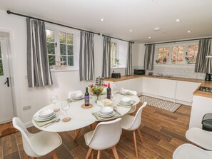 A modern kitchen with white cabinets, a wooden countertop, and a dining area with a round table set for four. - Willow Cottage (Sheffield)
