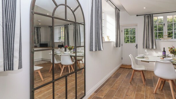 Un área de comedor moderna con un espejo grande, cortinas a rayas y vista a la cocina.