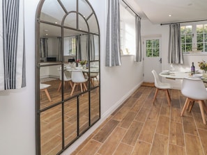 Un área de comedor moderna con un espejo grande, cortinas a rayas y vista a la cocina.