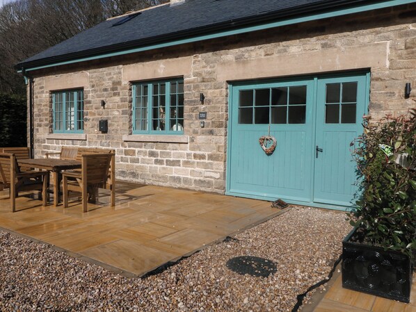A stone building with a teal door and windows, a wooden table and chairs outside, and a gravel path. - Willow Cottage (Sheffield)