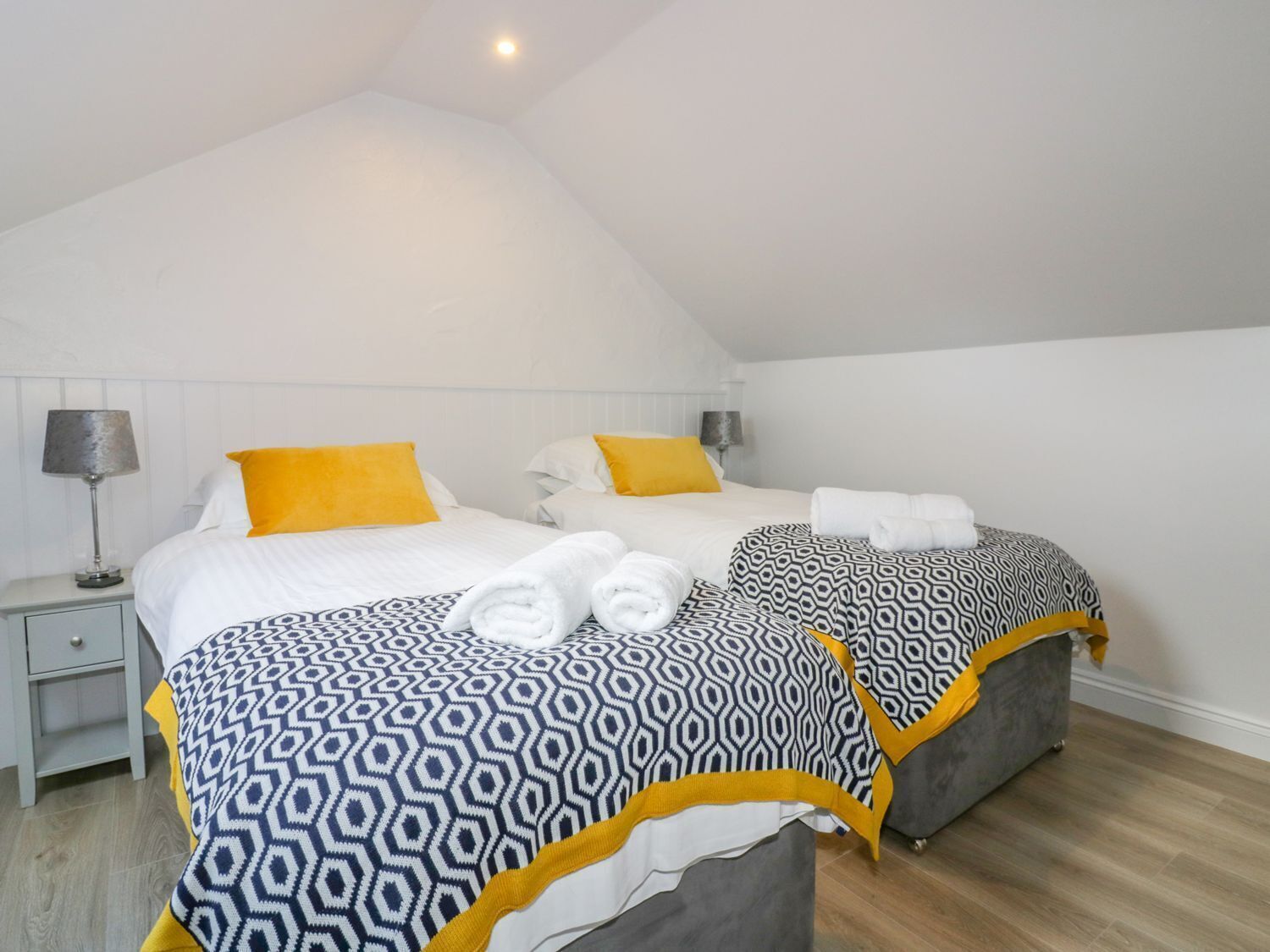 Un dormitorio con dos camas, cada una con ropa de cama estampada y almohadas amarillas. Hay dos mesitas de noche con lámparas.