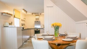 Una cocina moderna con armarios blancos, una mesa de comedor de madera para seis personas y un jarrón con flores amarillas.