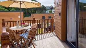 Una terraza de madera con una mesa, sillas, un paraguas y un ventanal de vidrio.