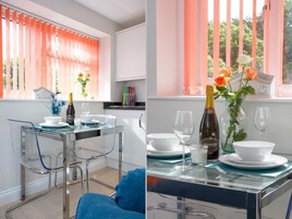 Un comedor moderno con una mesa de vidrio y sillas, una botella de Prosecco y un jarrón con flores.