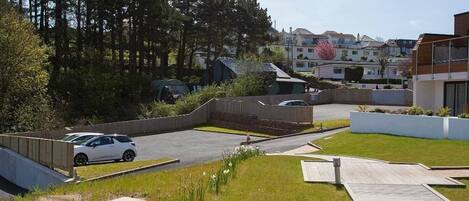 A residential area with a paved driveway, a white car parked, and houses in the background.