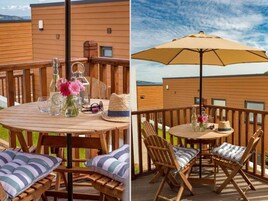 Una terraza de madera con una mesa redonda, sillas y un paraguas grande.