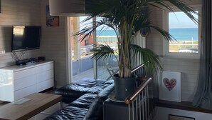 Un saló modern amb un finestra gran que dona al mar, un televisor de pantalla plana fixat a la paret i una planta en test amb un banc de fusta.