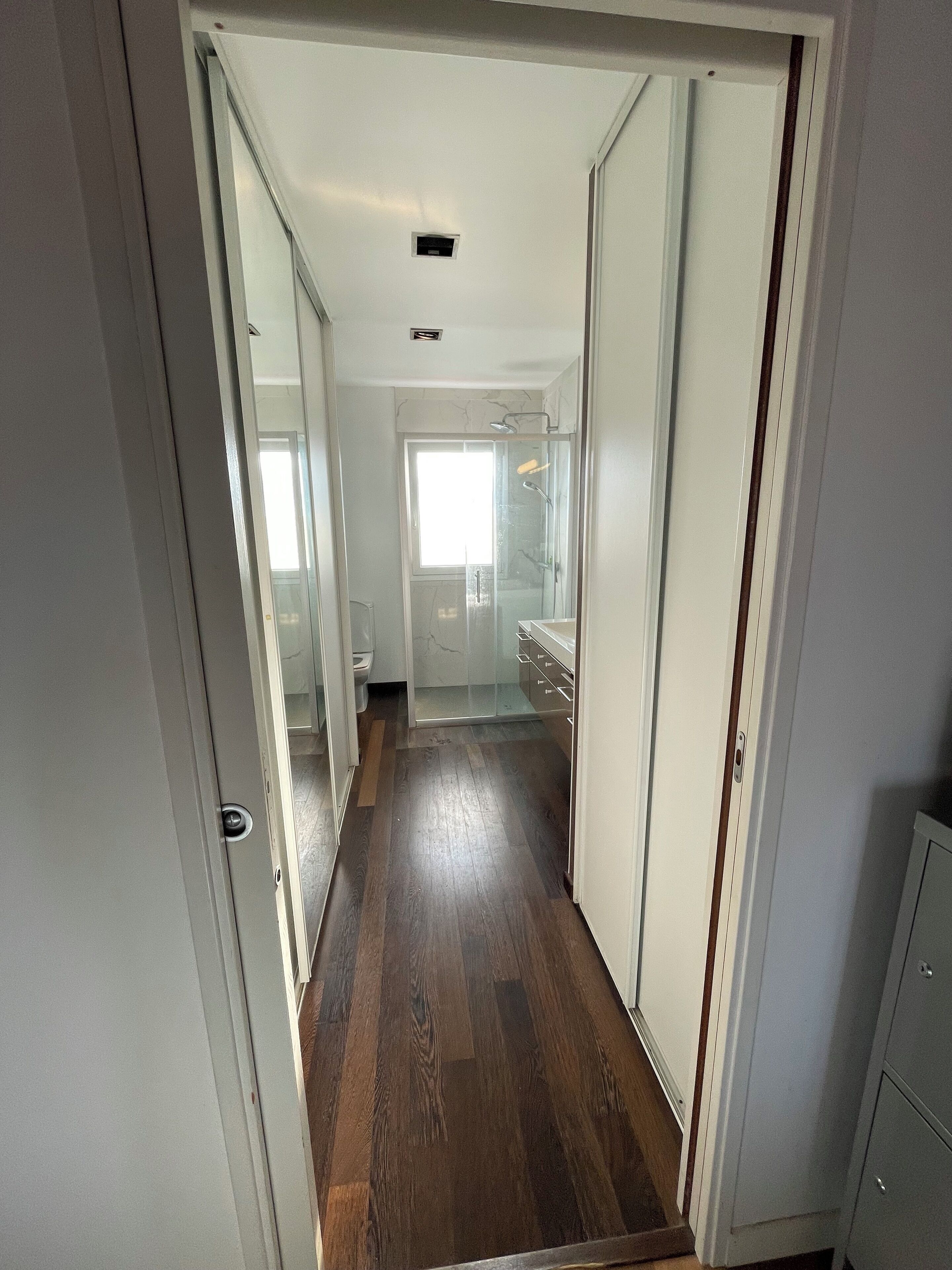 A hallway leading to a bathroom with a glass shower enclosure and a toilet visible in the background.