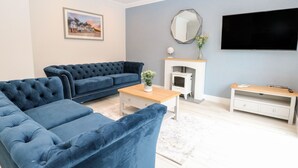 A living room with a blue sofa, a wooden coffee table, a fireplace, and a flat-screen TV mounted on the wall. - Harbour Place (Wells-next-the-Sea)