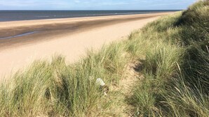 A beach with sand and grass in the foreground. - Harbour Place (Wells-next-the-Sea)