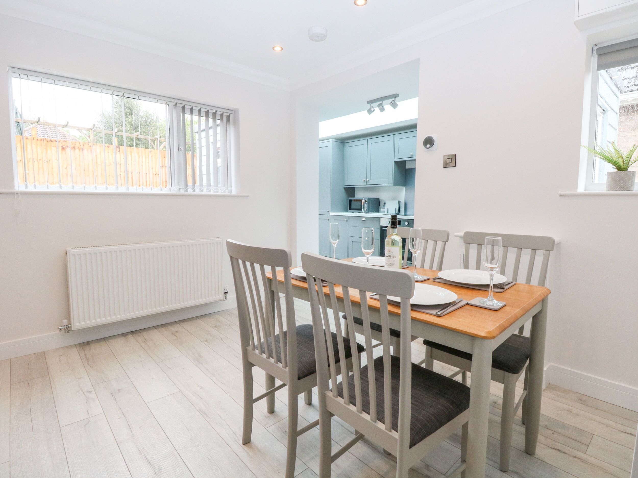 A dining area with a table set for four, white chairs, a wooden table, and a view into a kitchen with blue cabinets.
