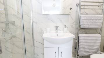 A bathroom with a glass-enclosed shower, a white sink with a mirror above it, and a towel rack with two towels.