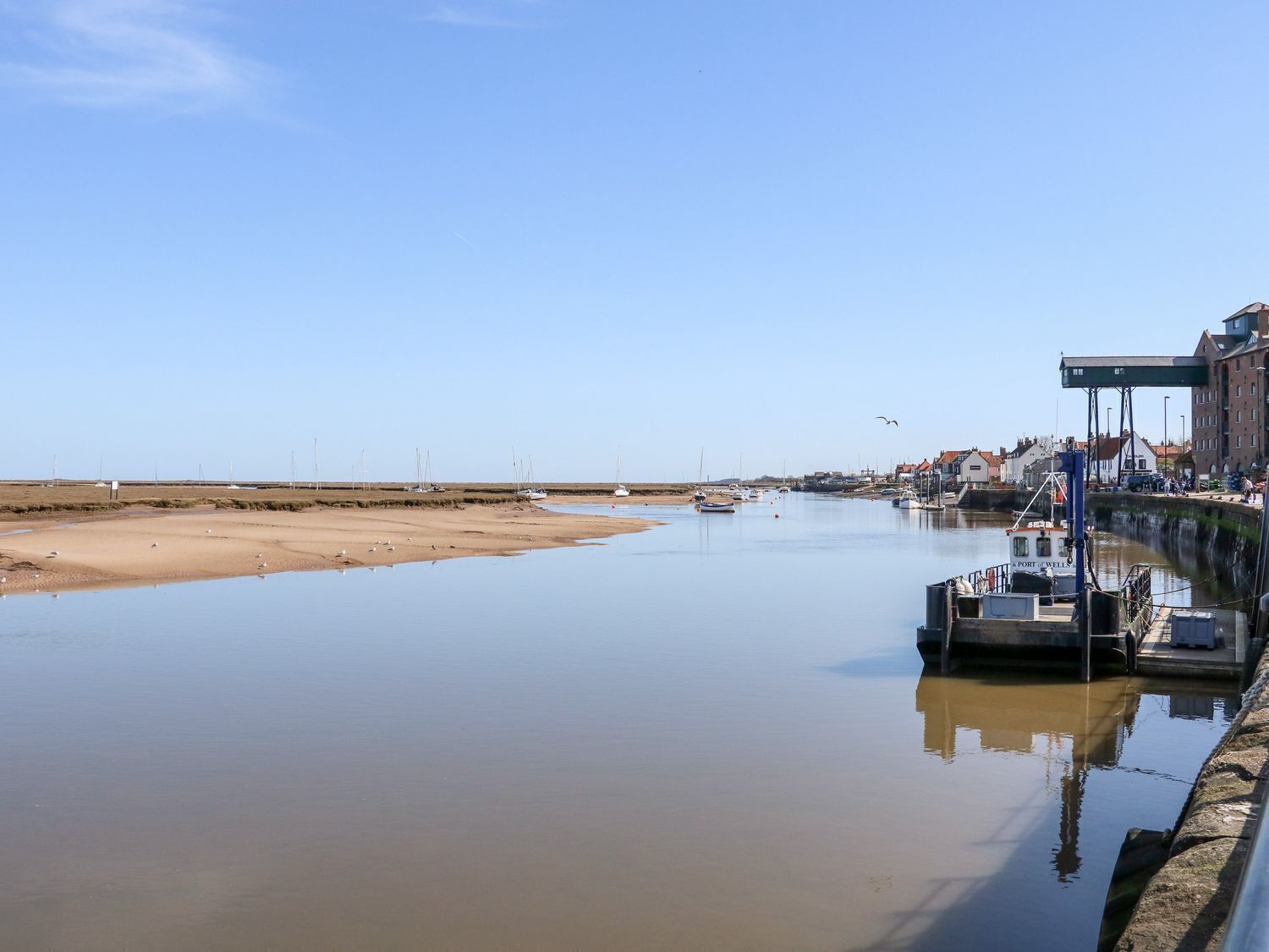 Ruhiger Hafen mit Booten, einer Anlegestelle und Gebäuden im Hintergrund.