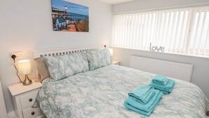 Quarto com cama, mesa de cabeceira, luminária, quadro na parede e janela com persianas.