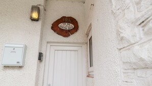 Uma porta branca com puxador de metal, uma parede branca texturizada, uma placa de madeira acima da porta com a inscrição "19A The Old Counting House" e uma pequena caixa elétrica branca à esquerda.