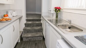 Cozinha moderna com armários brancos, bancada de granito, torradeira, chaleira, pia e um vaso com flores.