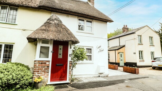 A white house with a red door, a thatched roof, and a brick wall.