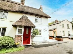 A white house with a red door, a thatched roof, and a brick wall. - Cosynook Cottage (Blandford Forum)