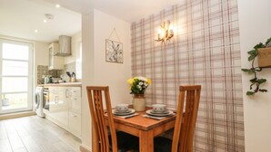 A dining area with a wooden table, two chairs, a vase with flowers, and a plaid-patterned wall.