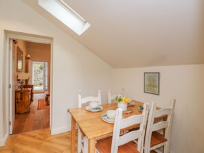 Un coin repas avec une table en bois et des chaises blanches, un vase rempli de fleurs et un tableau accroché au mur.