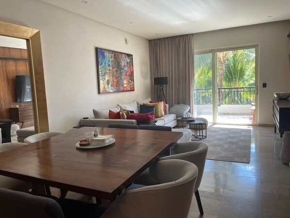 A spacious living area with a dining table, sofa, and a large window with a view of greenery.