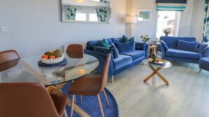 A modern living room with a glass dining table, blue sofas, and a large mirror. - Ocean View Apartment (Colwyn Bay)