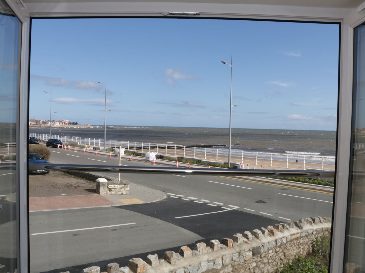 Een kustweg met een stenen muur, een voetpad en uitzicht op strand en zee.