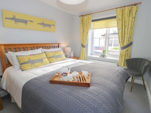 A neatly made bed with a tray of breakfast items, a wooden headboard, a chair, and a window with curtains. - Ocean View Apartment (Colwyn Bay)