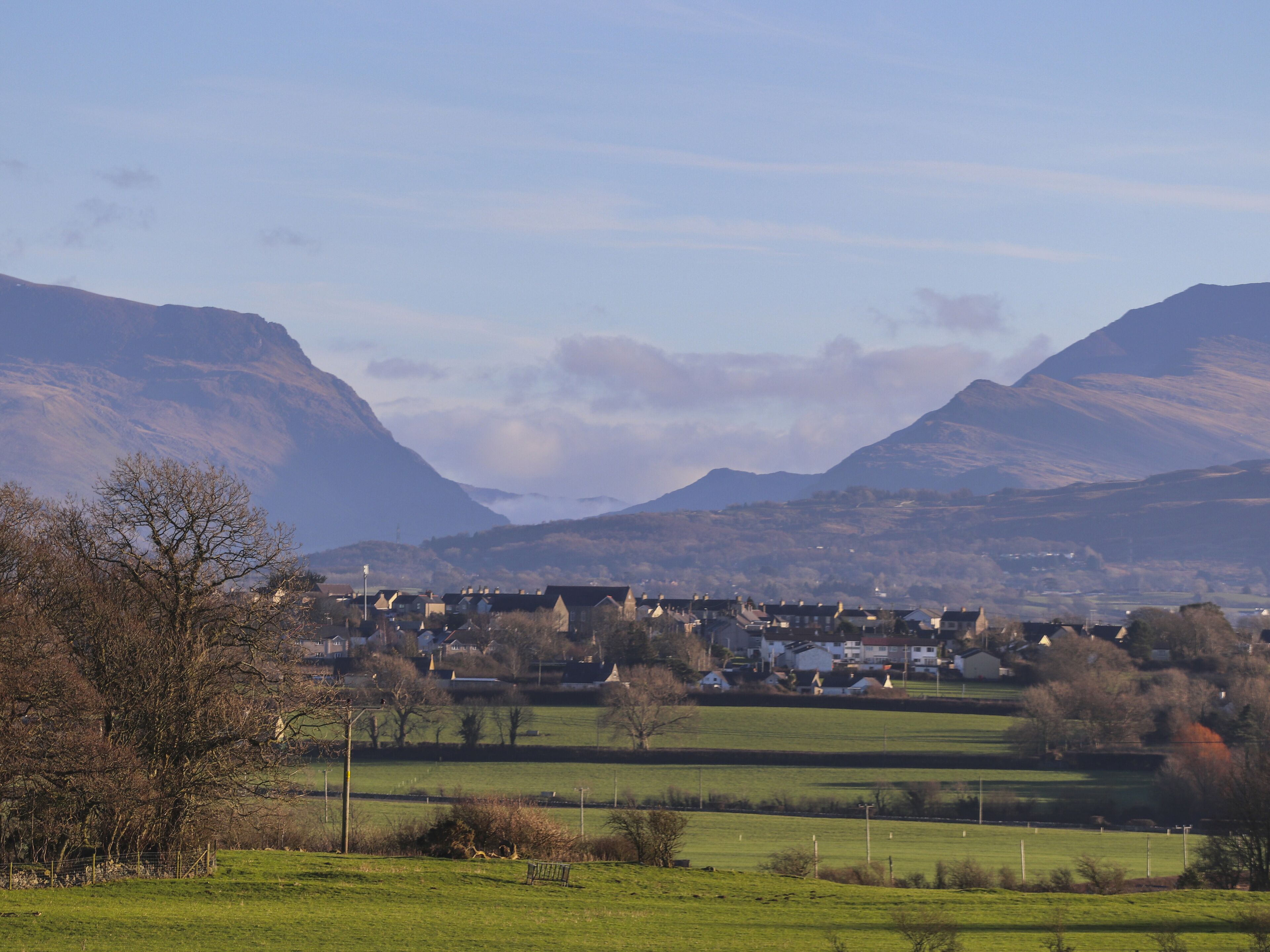 A rural landscape with houses, a grassy field, and mountains in the background.