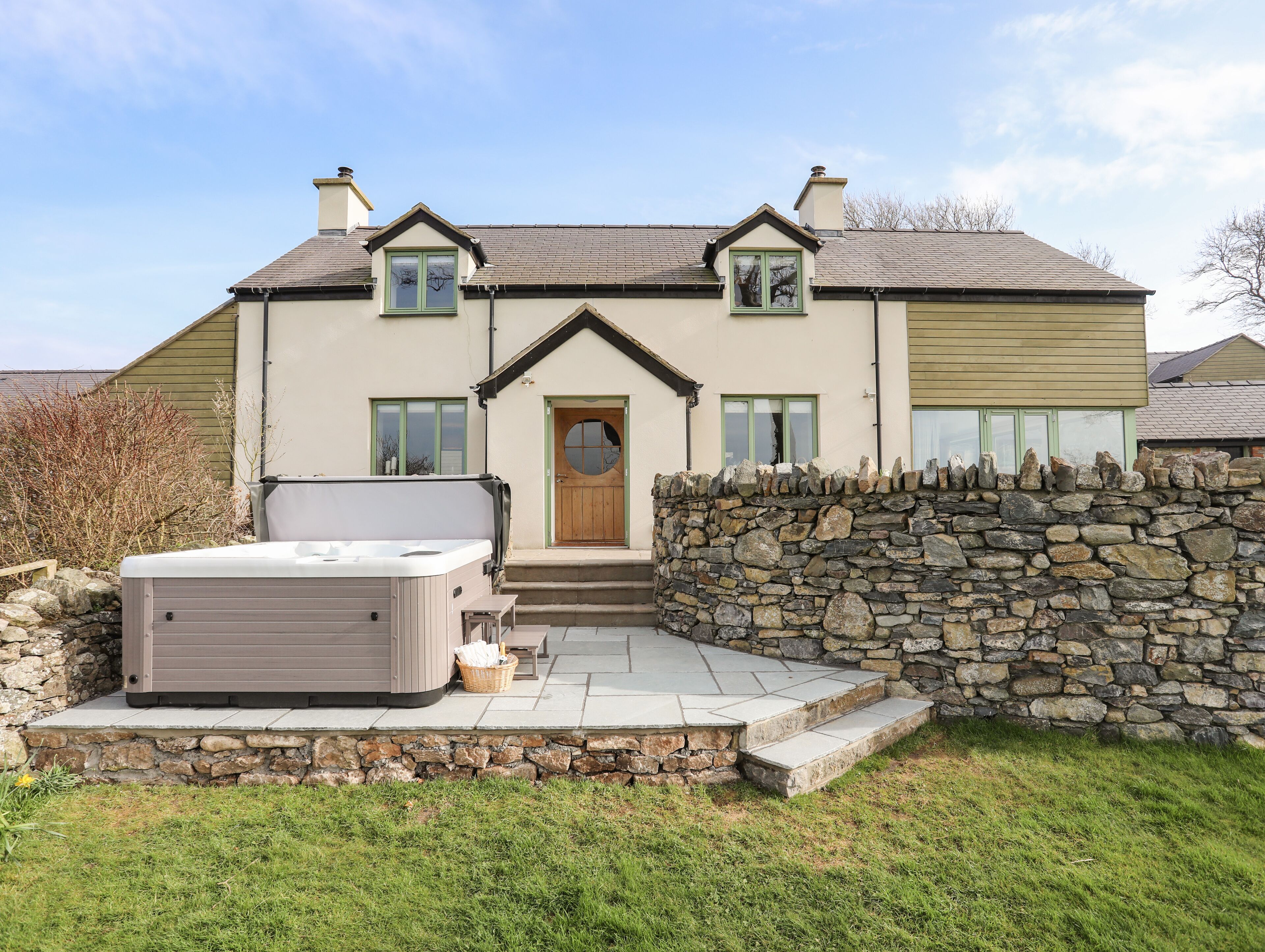 A two-story house with a stone wall and a hot tub in the front yard.
