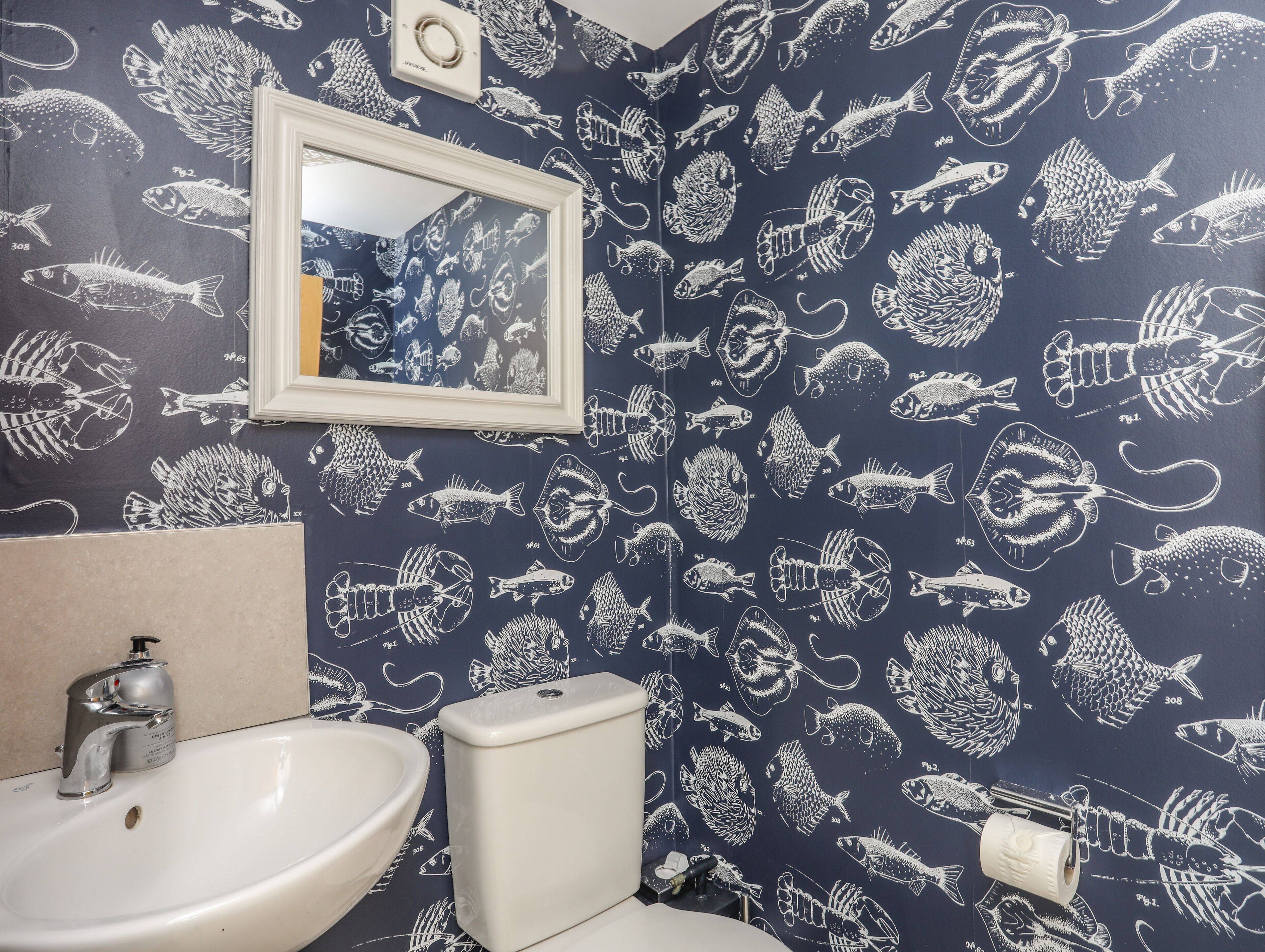 A bathroom with a sink, toilet, and mirror. The walls are decorated with a pattern of fish and marine life.