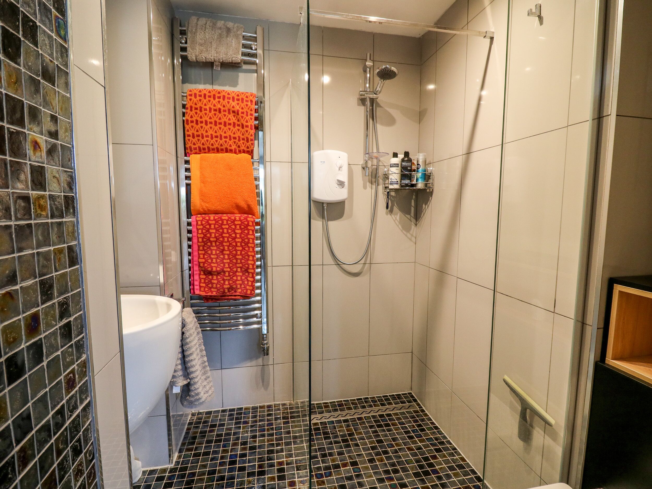 A modern bathroom with a glass shower enclosure, a white sink, and a tiled floor.