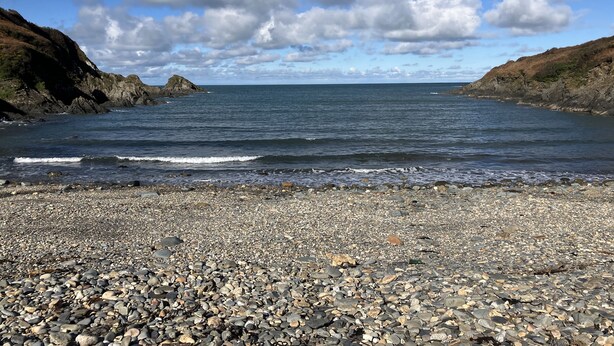 A rocky beach with a calm sea and distant rocky cliffs under a partly cloudy sky. - Dolwern (Newport)