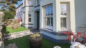 A two-story house with a stone foundation, a well-maintained lawn, and a wooden barrel planter. - Dolwern (Newport)