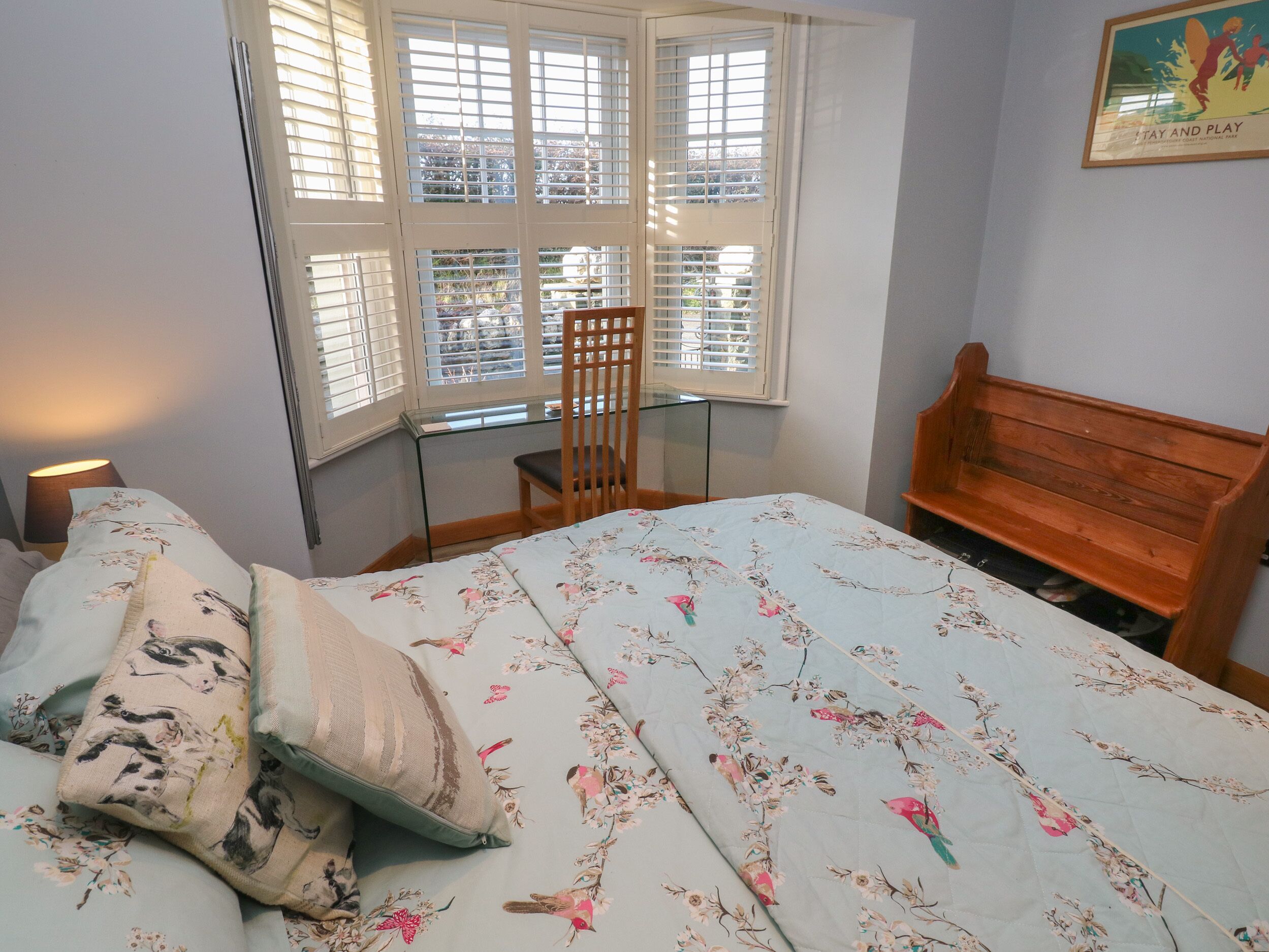 A bedroom with a bed, a wooden bench, a chair, and a desk near a window with blinds.