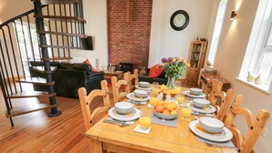 A dining area with a wooden table set for six, surrounded by wooden chairs. A brick wall and a clock are visible in the background. - The Old Church (York)