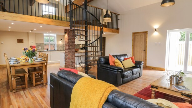 A spacious living area with a black leather sofa, a dining table with chairs, a staircase, and a kitchen in the background. - The Old Church (York)