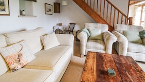 Ein gemütliches Wohnzimmer mit einer Holztreppe, einem Sofa, einem Sessel und einem Couchtisch.