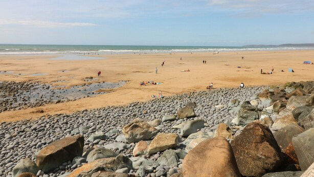 Uma praia com um primeiro plano rochoso e uma área de praia arenosa.