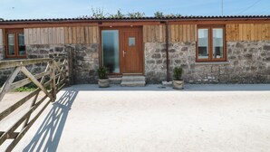 A rustic building with a wooden facade, a stone wall, and a metal gate. - The Old Cow Shed (Banwell)