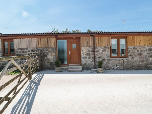A rustic building with a wooden facade, a stone wall, and a metal gate. - The Old Cow Shed (Banwell)