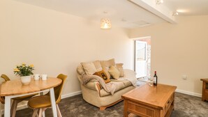 A cozy living room with a round wooden table, a beige sofa, and a small wooden side table. - The Old Cow Shed (Banwell)