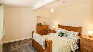 A bedroom with a wooden bed, a nightstand, a dresser, and a ceiling light fixture. - The Old Cow Shed (Banwell)