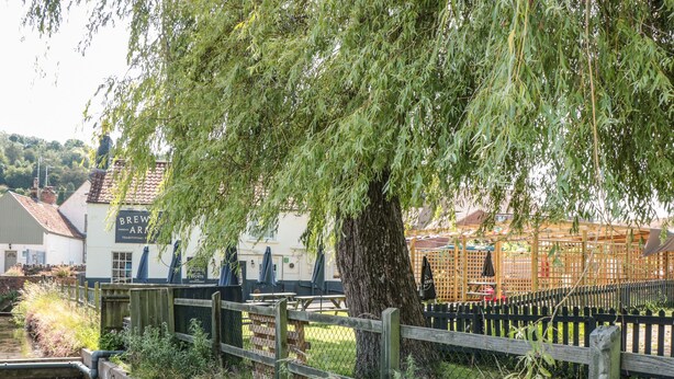 A riverside view with a wooden fence, a tree, and a building labeled "BREWERY ARMS". - The Old Cow Shed (Banwell)