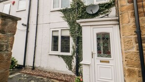 A white house with a stone facade, a satellite dish, and a door with a glass panel. - Swainby Cottage (Northallerton)